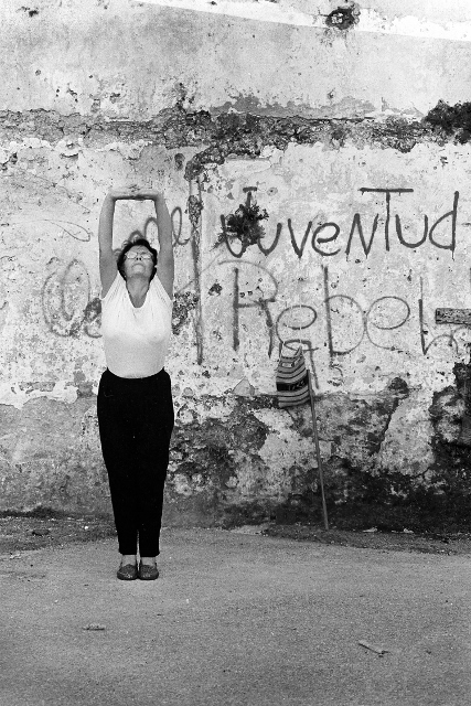 Black and white photo of an older woman stretching both arms overhead. 